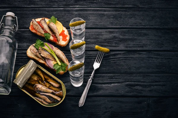 Vodka and a set of sandwiches with sprats, and caviar, onion and parsley, on a wooden background. Top view. Copy space. — Stock Image Vodka Set Sandwiches Sprats Caviar Onion Parsley Wooden Background Top Stock Photo