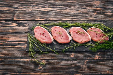 Çiğ et. Biberiye ve baharat siyah ahşap zemin sığır eti biftek. Üstten Görünüm. Metin için boş alan.