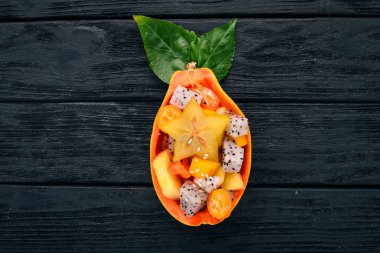 Tropikal meyve salatası servis yarım bir Papaya. Dragon meyve, rambutan, demirhindi, kaktüs meyve, avokado, mango. Ahşap bir arka plan üzerinde. Üstten Görünüm.