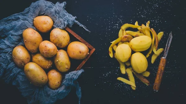 Raw potatoes on a black wooden background. Cooking. Free space for text. Top view.