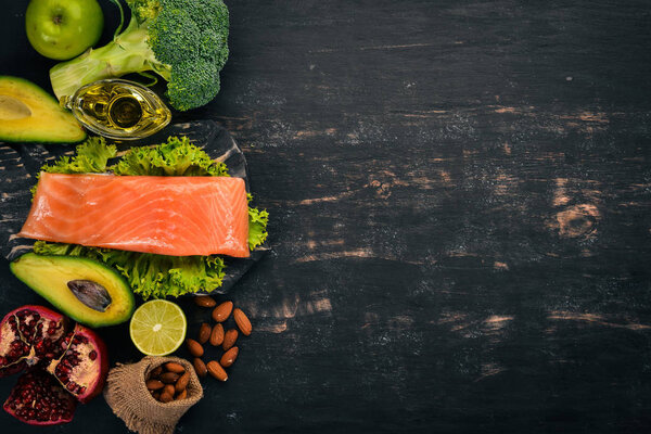 Здоровое питание. Рыбный лосось, авокадо, брокколи, свежие овощи, орехи и фрукты. На черном фоне. Вид сверху. Копирование пространства
.