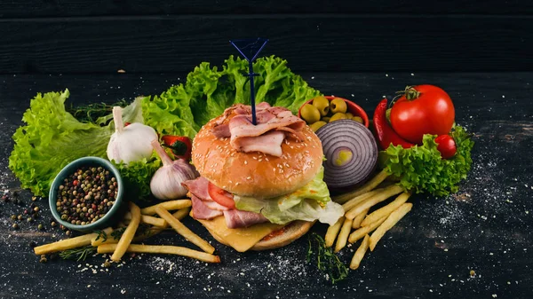 Burger with bacon, cheese and lettuce. American Traditional Food. On a black wooden background. Copy space.