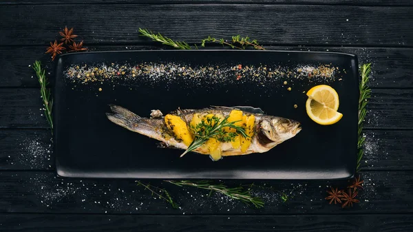 Fish sibas baked with vegetables and citrus fruits. On a black wooden background. Copy space.