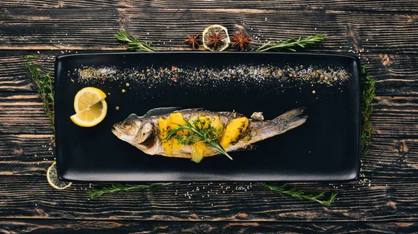 Fish sibas baked with vegetables and citrus fruits. On a black wooden background. Copy space.