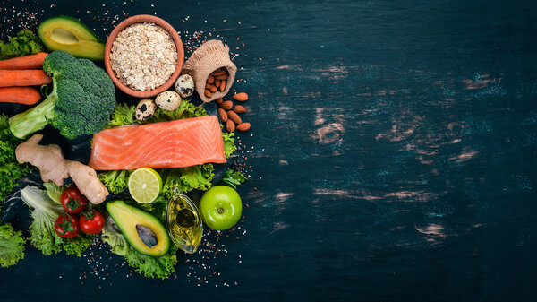 Healthy food. Fish salmon, avocado, broccoli, fresh vegetables, nuts and fruits. On a black background. Top view. Copy space.