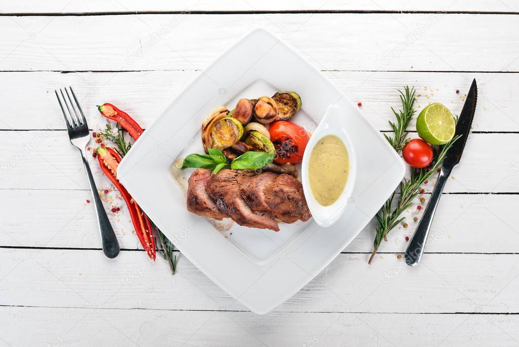 Pork steak with grilled vegetables on a plate. On a wooden background. Top view. Copy space.