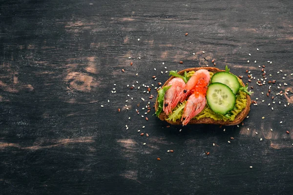 Burger, sandwich with shrimp, avocado, caviar and cucumber. On a wooden background. Top view. Copy space.