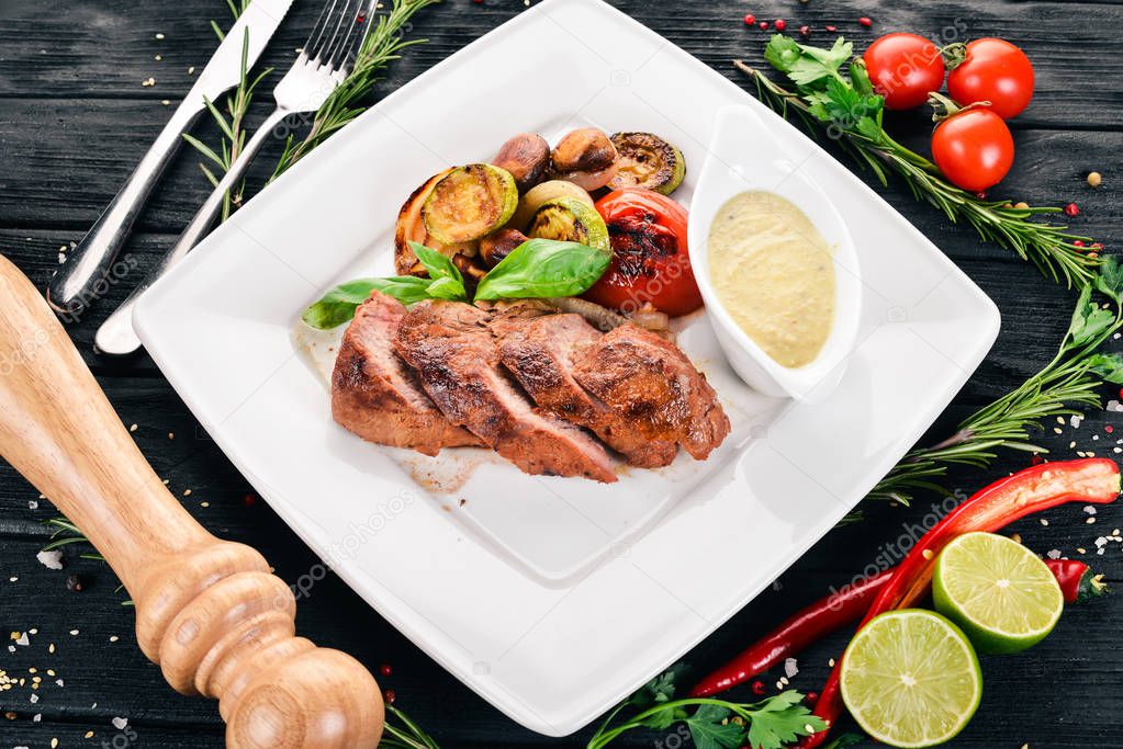 Pork steak with grilled vegetables on a plate. On a wooden background. Top view. Copy space.