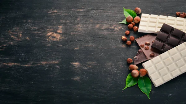 A set of milk chocolate and black chocolate hazelnuts. On a black wooden background. Copy space for text.