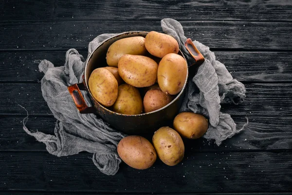 Raw potatoes on a black wooden background. Cooking. Free space for text. Top view.