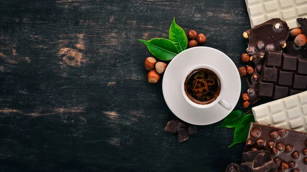 A cup of coffee and a set of chocolate with cookies and sweets. On a black wooden background. Top view. Copy space for text.