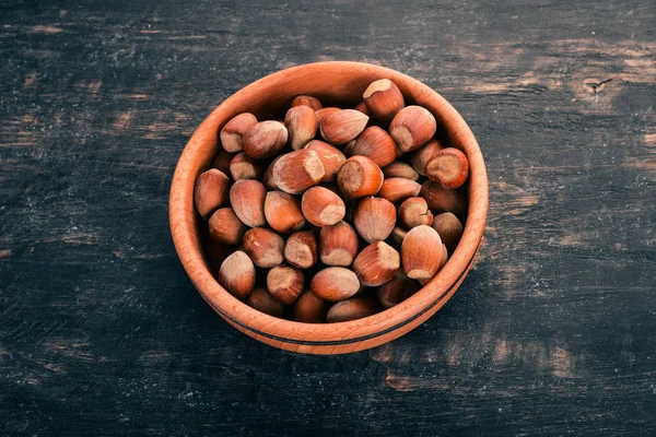 Hazelnut in a wooden bowl. On a black wooden background. Top view. Copy space for your text.