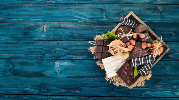 一组牛奶巧克力和黑巧克力 装在一个有坚果和饼干的木箱里 在蓝色的木质背景上 复制文本空间 — 图库照片