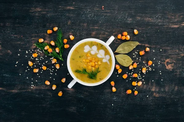 Corn soup with fresh vegetables in a bowl. Healthy food. On a black wooden background. Top view. Copy space for your text.