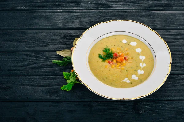 Corn soup with fresh vegetables in a bowl. Healthy food. On a black wooden background. Top view. Copy space for your text.