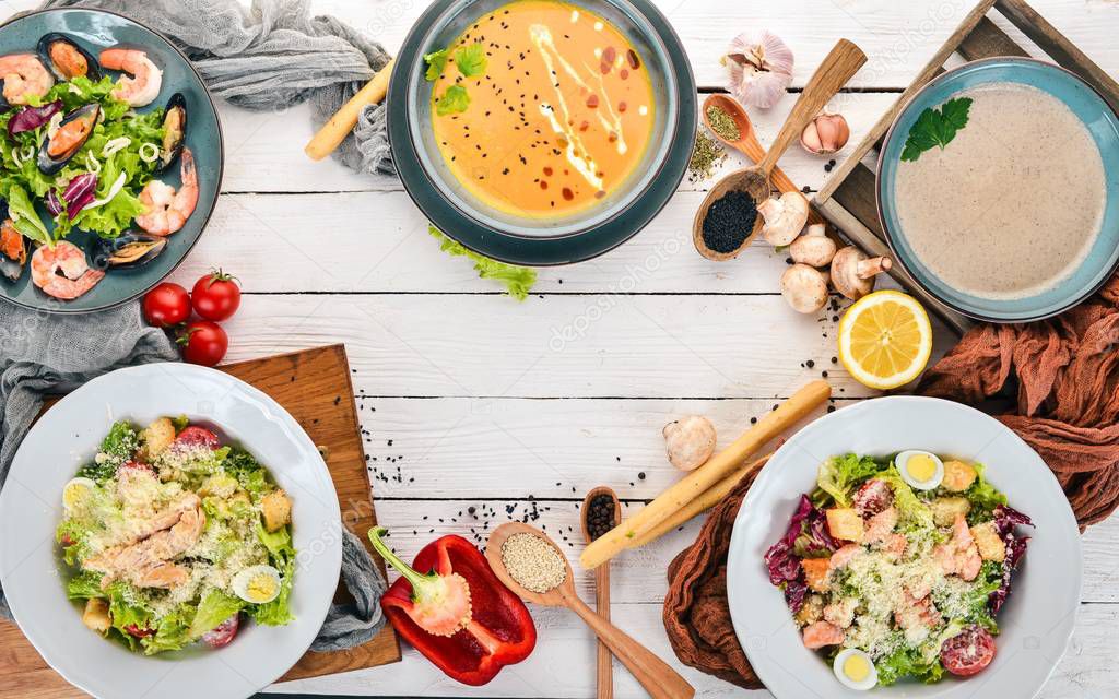 A set of healthy food in plates. Caesar salad, seafood, pumpkin soup and mushrooms. Top view. On a wooden background. Copy space.
