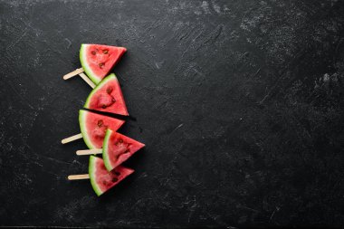 Siyah arka planda karpuz dondurması. Çubuklarda karpuz dilimleri. Üst Manzara. Boş kopyalama alanı.