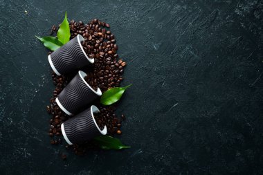 Kahve ve kahve çekirdeği için kağıt bardaklar. Siyah taştan bir arka planda. Üst Manzara. Metnin için boş yer.