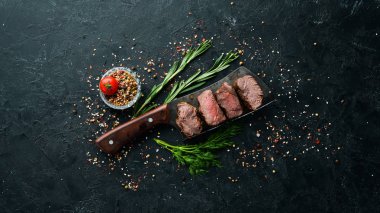Bıçaklı biftek, siyah taşlı arka plan. Üst Manzara. Metnin için boş yer.