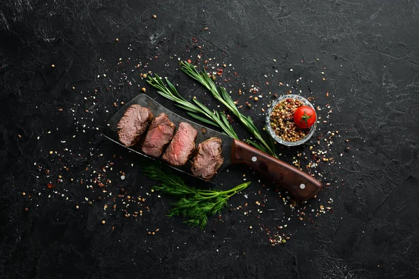 Beef steak on knife, on black stone background. Top view. Free space for your text.