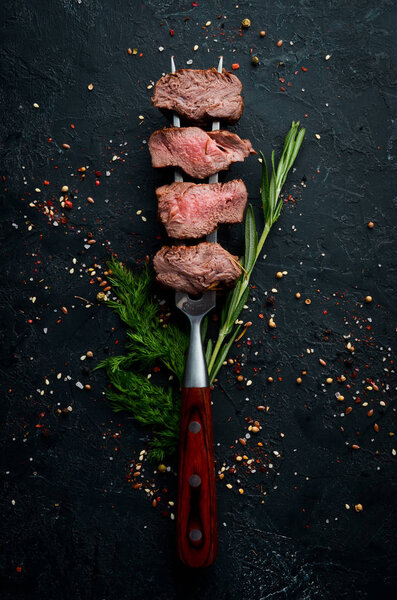 Baked veal on a fork. Veal steak on black stone background. Top view. Free space for your text.