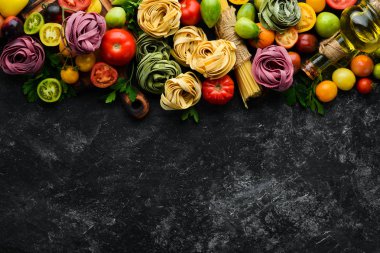 Makarna arka planı. Kuru makarna tagliatelle ve siyah arka planda malzemeler. Üst Manzara. Metnin için boş yer.