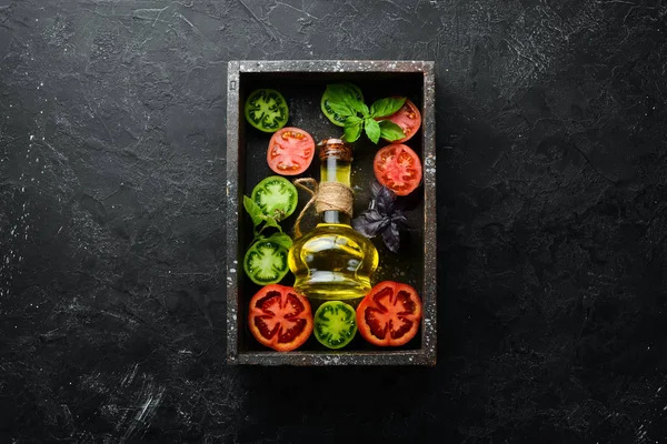 Ahşap bir kutuda yağ dolu renkli domatesler. Siyah taştan bir arka planda. Üst Manzara. Metnin için boş yer.