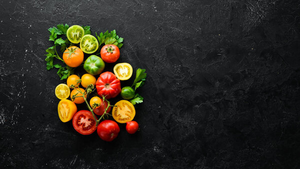 Vegetables. Fresh colored tomatoes On a black stone background. Top view. Free space for your text.