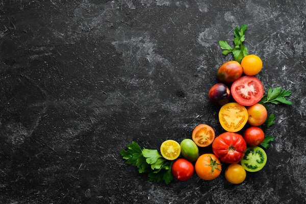 Vegetables. Fresh colored tomatoes On a black stone background. Top view. Free space for your text.