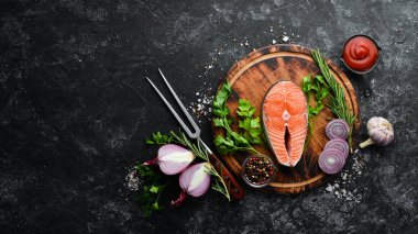 Siyah taşlı arka planda somon bifteği ve malzemeler. Üst Manzara. Metnin için boş yer.