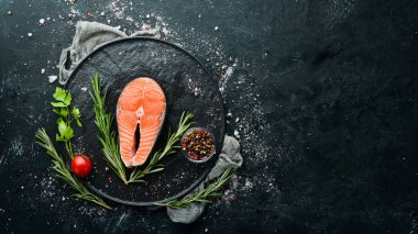 Siyah taşlı arka planda somon bifteği ve malzemeler. Üst Manzara. Metnin için boş yer.