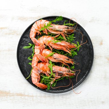 Siyah bir tabakta kaynamış karides ve roka. Deniz ürünleri tabakları. Üst Manzara. Metnin için boş yer.