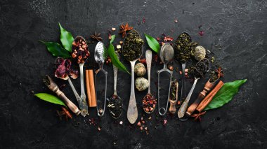 Kaşıklara çay koy. Siyah, yeşil, meyve ve beyaz çay. Siyah taştan bir arka planda. Üst Manzara. Metnin için boş yer.