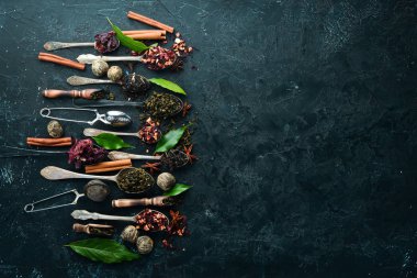 Kaşıklara çay koy. Siyah, yeşil, meyve ve beyaz çay. Siyah taştan bir arka planda. Üst Manzara. Metnin için boş yer.