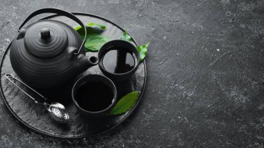 Çaydanlık ve siyah taştan bir arka planda iki fincan çay. Üst Manzara. Metnin için boş yer.