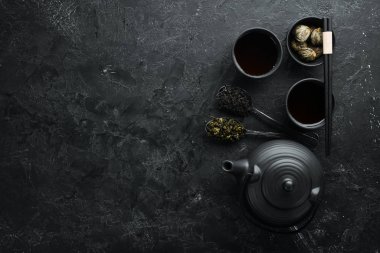 Çaydanlık ve siyah taştan bir arka planda iki fincan çay. Üst Manzara. Metnin için boş yer.