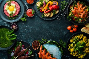 Siyah bir arka planda çeşitli yiyecek ve sebze, et ve balık tabakları. Üst Manzara. Metnin için boş yer.