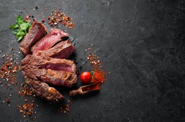 Siyah taşlı arka planda dilimlenmiş biftek. Siyah Angus. Üst Manzara. Metnin için boş yer. Kırsal biçim.