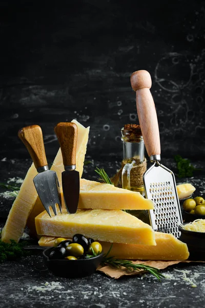 Set of hard cheeses with cheese knives on black stone background. Parmesan. Top view. Free space for your text.