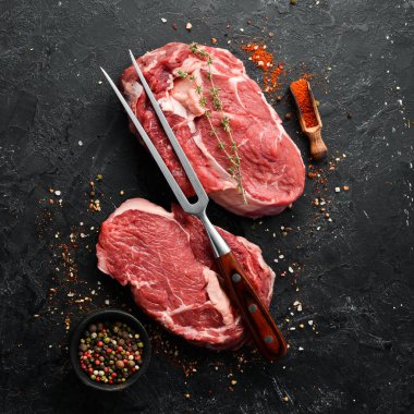 Siyah taşlı arka planda çatalı olan çiğ biftekli siyah Angus. Üst Manzara. Metnin için boş yer. Kırsal biçim.