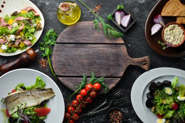 Yiyecekler. Siyah taş arka planda salata ve tabaklar. Üst Manzara. Metnin için boş yer. Kırsal biçim.