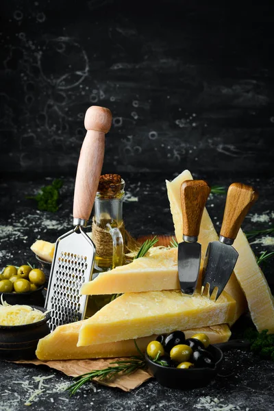 Hard cheese with olives and cheese knife on black stone background. Parmesan. Top view. Free space for your text.