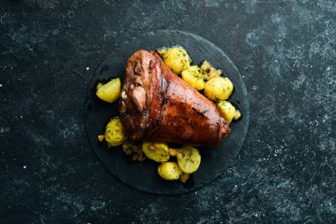 Baked pork leg with potatoes on a black stone plate. Pepper steak. Top view, free space for your text. Rustic style.