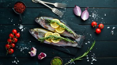 Siyah ahşap arka planda sebze li çiğ balık. Balık alabalığı. Üst te. Metniniz için boş alan.