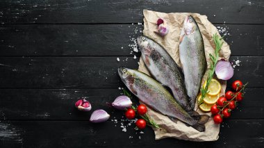 Siyah ahşap arka planda sebze li çiğ balık. Balık alabalığı. Üst te. Metniniz için boş alan.