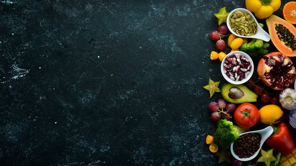Organic food. Fruits, vegetables, beans and nuts on a black stone background. Top view. Free space for your text.