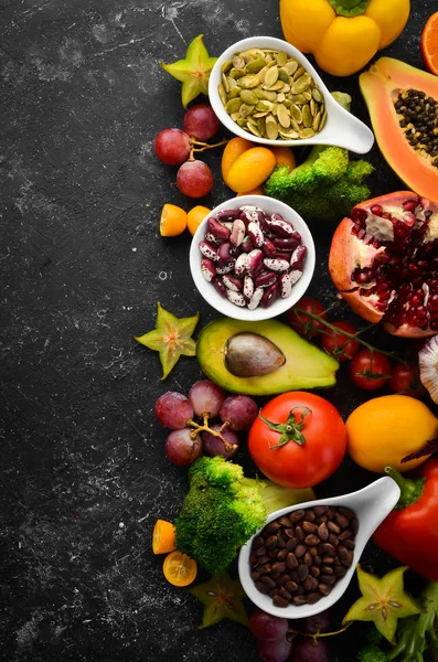 Organic food. Fruits, vegetables, beans and nuts on a black stone background. Top view. Free space for your text.