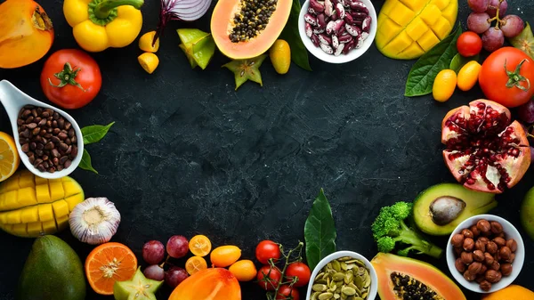 Organic food. Fruits, vegetables, beans and nuts on a black stone background. Top view. Free space for your text.