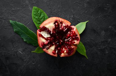 Siyah taş arka planda yaprakları olan taze nar. Meyveler. Üst Manzara. Metnin için boş yer.