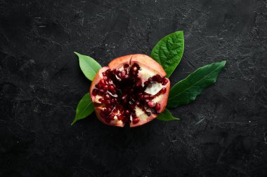 Siyah taş arka planda yaprakları olan taze nar. Meyveler. Üst Manzara. Metnin için boş yer.